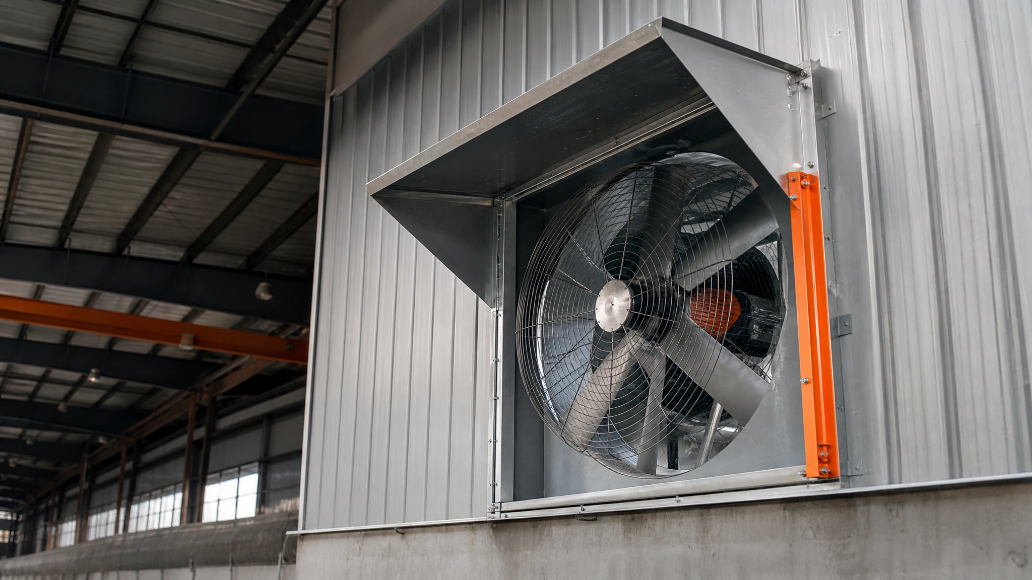 Large industrial exhaust fan mounted in a high-bay factory opening with weather hood